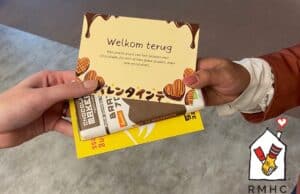 2 handen die een kaartje en chocolade van elkaar aannemen